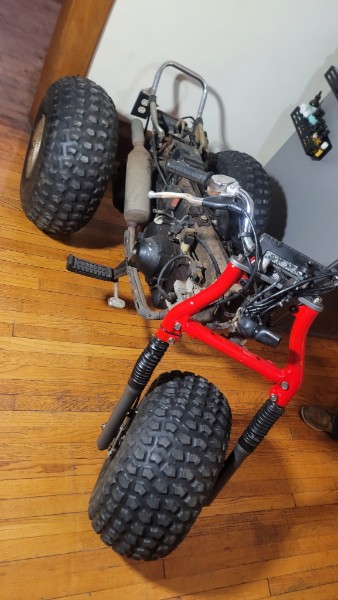 Honda ATC 70 being reassembled on the living room floor — all three wheels back on, red frame visible with engine going back in