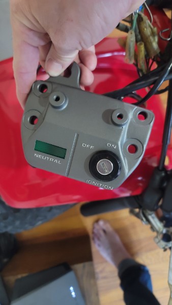Restored Honda ATC 70 ignition panel installed on the machine, held in hand showing the clean matte gray finish against the red bodywork