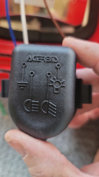Acerbis headlight switch held in hand showing the illuminated icons for ground, parking light, low beam, and high beam