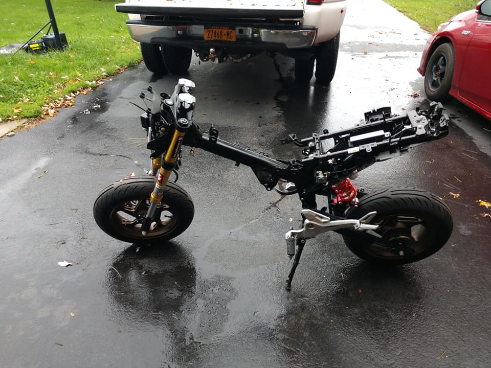 Honda Grom bare rolling chassis with gold inverted forks and red rear shock sitting outside in the rain on a driveway
