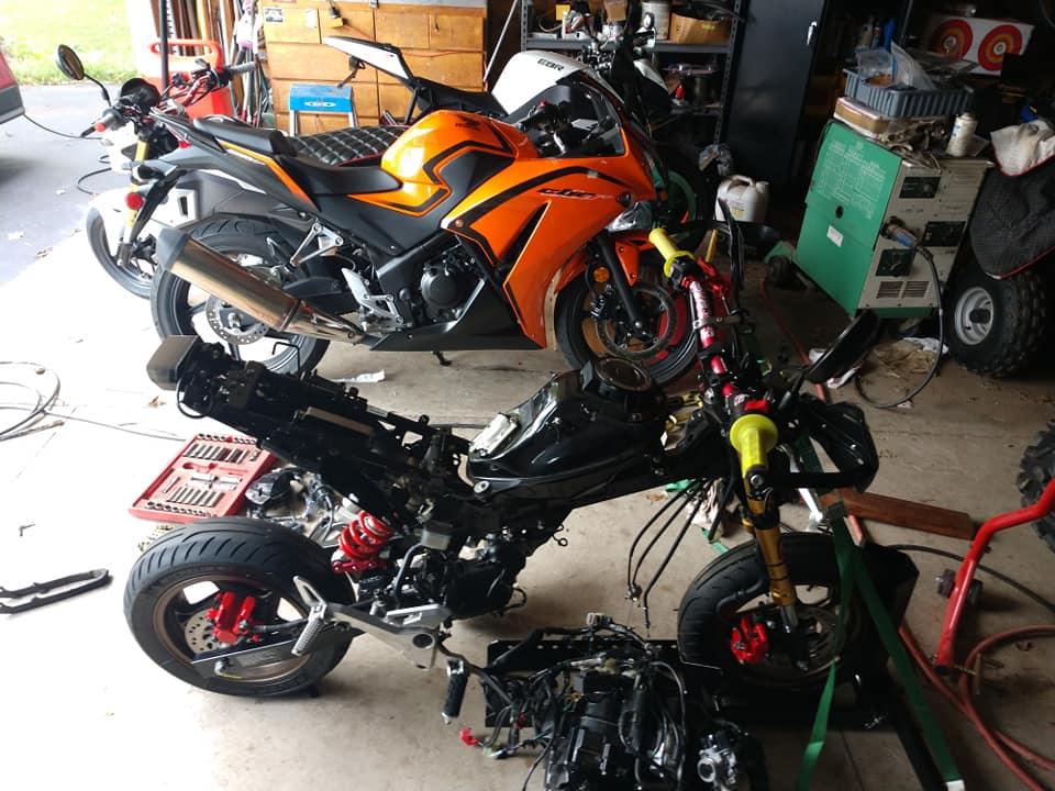Honda Grom completely stripped to bare frame and wiring on the garage floor, next to a full-size CBR sport bike for scale