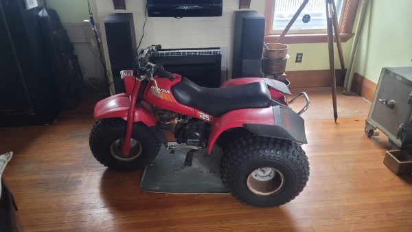 Red Honda ATC 125 three-wheeler in a living room, stock condition, ready for inspection — what a running 125 looks like