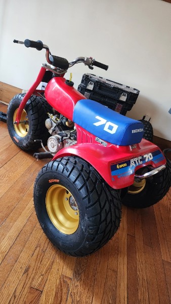 Rear three-quarter view of the completed Honda ATC 70 restoration showing the rear axle, gold wheels, and Honda ATC 70 side decals on red bodywork